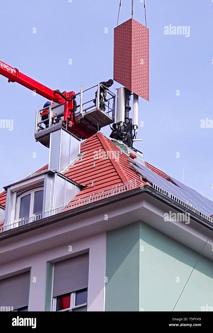 02 April 2019, Bavaria, Würzburg: Workers dress up a mobile phone transmitter with a dummy chimney on a residential and commercial building. Photo: Kilian Moritz/dpa Stock Photo
