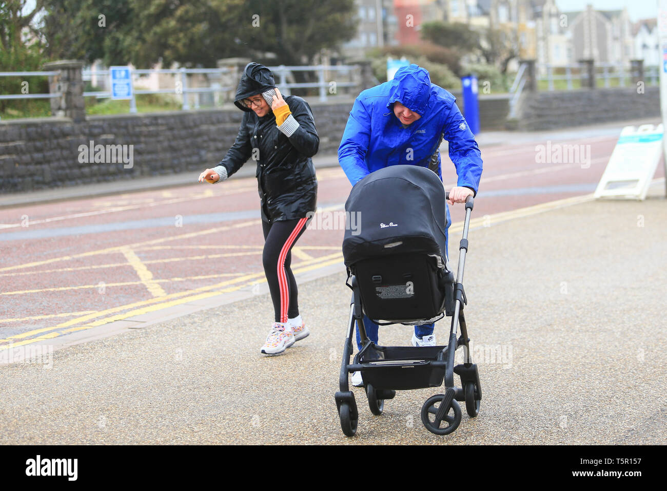 Weston-Super-Mare, Somerset, UK. 27th April,2019. A young couple with a pushchair struggle through the high wind on Weston's seafront. Peter Lopeman/Alamy Live News Stock Photo