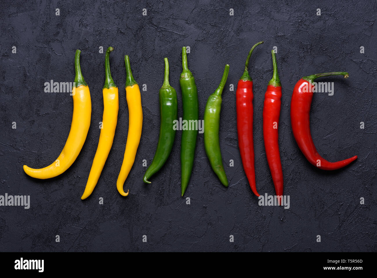 Different colored chilli peppers sorted by color on dark stone background Stock Photo