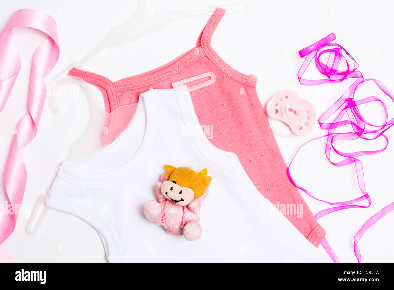 Two pink and whie babysuits with toy, pacifier and ribbons. Baby shower decoration on whie background. Flat lay style. Newborn girl clothes. Top view Stock Photo