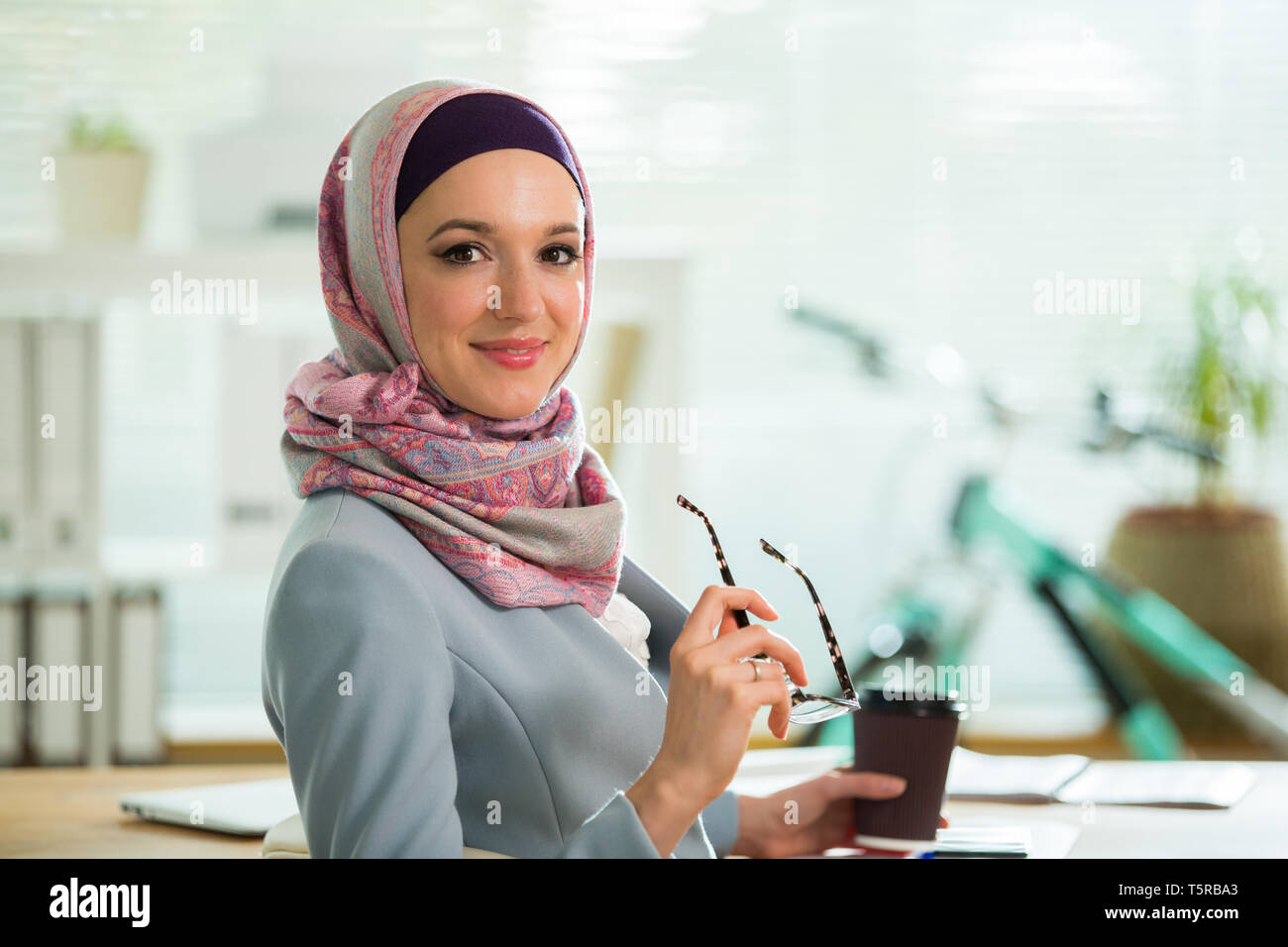 Beautiful stylish woman in hijab and eyeglasses, sitting at desk with ...