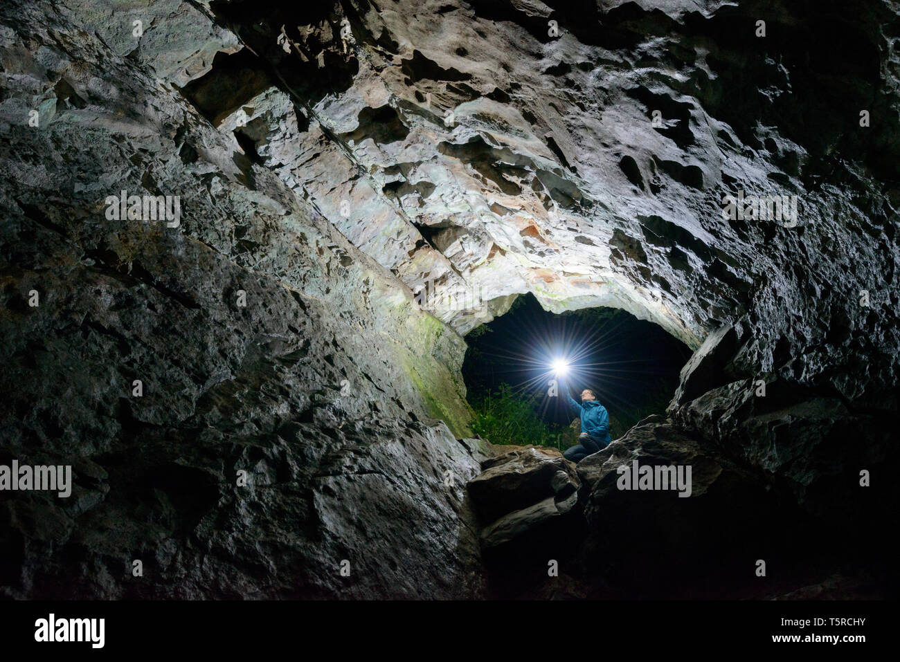A woman shines a torch into the entrance of Aveline's Hole, a cave on