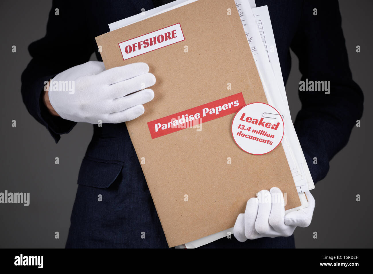 Man in suit and white gloves hold paper folder with Paradise Papers and Offshore label with documents inside, tax heaven documents leak concept Stock Photo
