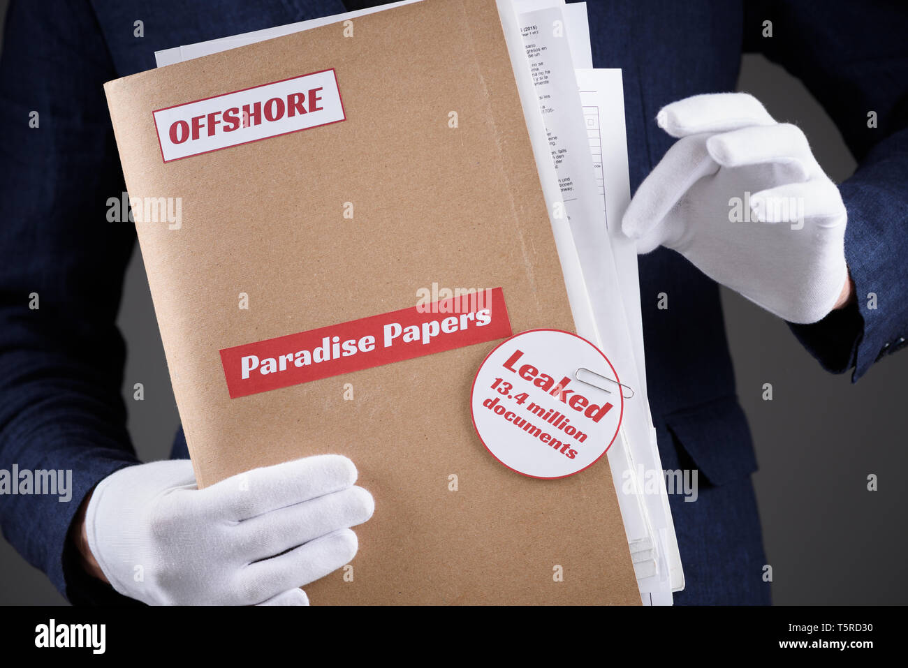 Man in white gloves hold paper folder with Paradise Papers and Offshore label with documents inside, and pull one out, tax heaven documents leak conce Stock Photo