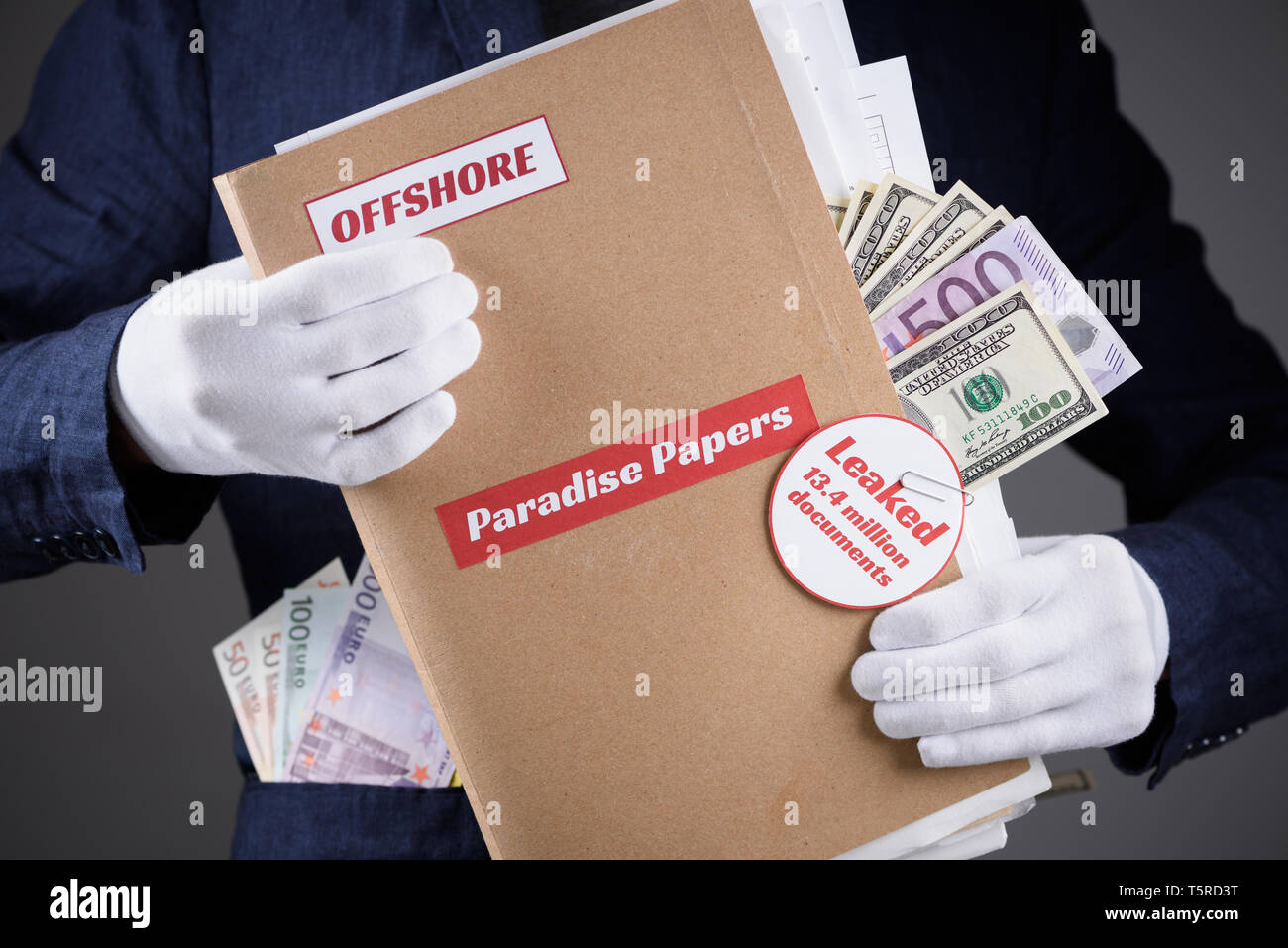 Man in suit with euro and dollar currency in pokets and in white gloves hold paper folder with Paradise Papers and Offshore label with documents insid Stock Photo