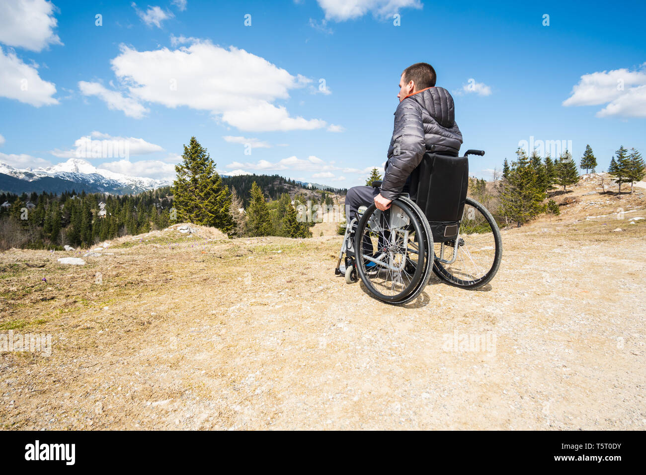 Young disabled man in wheelchair outside in nature observing mountains ...