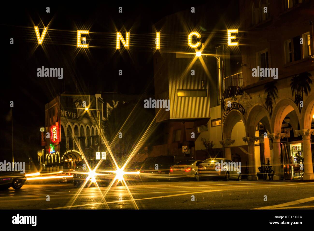 Illuminated street sign over cars' starburst lights mark entrance to Venice Beach, California Stock Photo