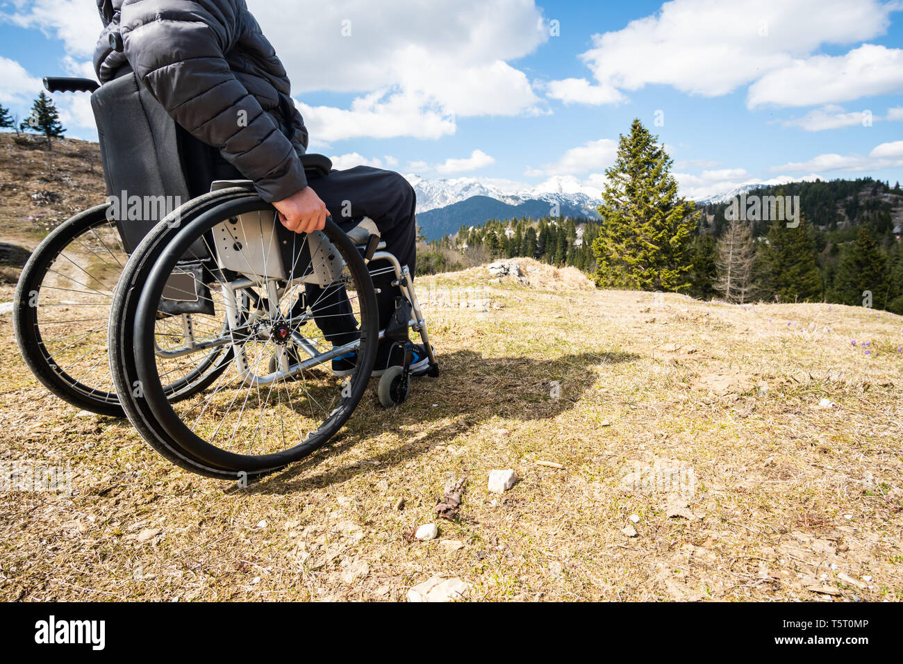 Young disabled man in wheelchair outside in nature observing mountains ...
