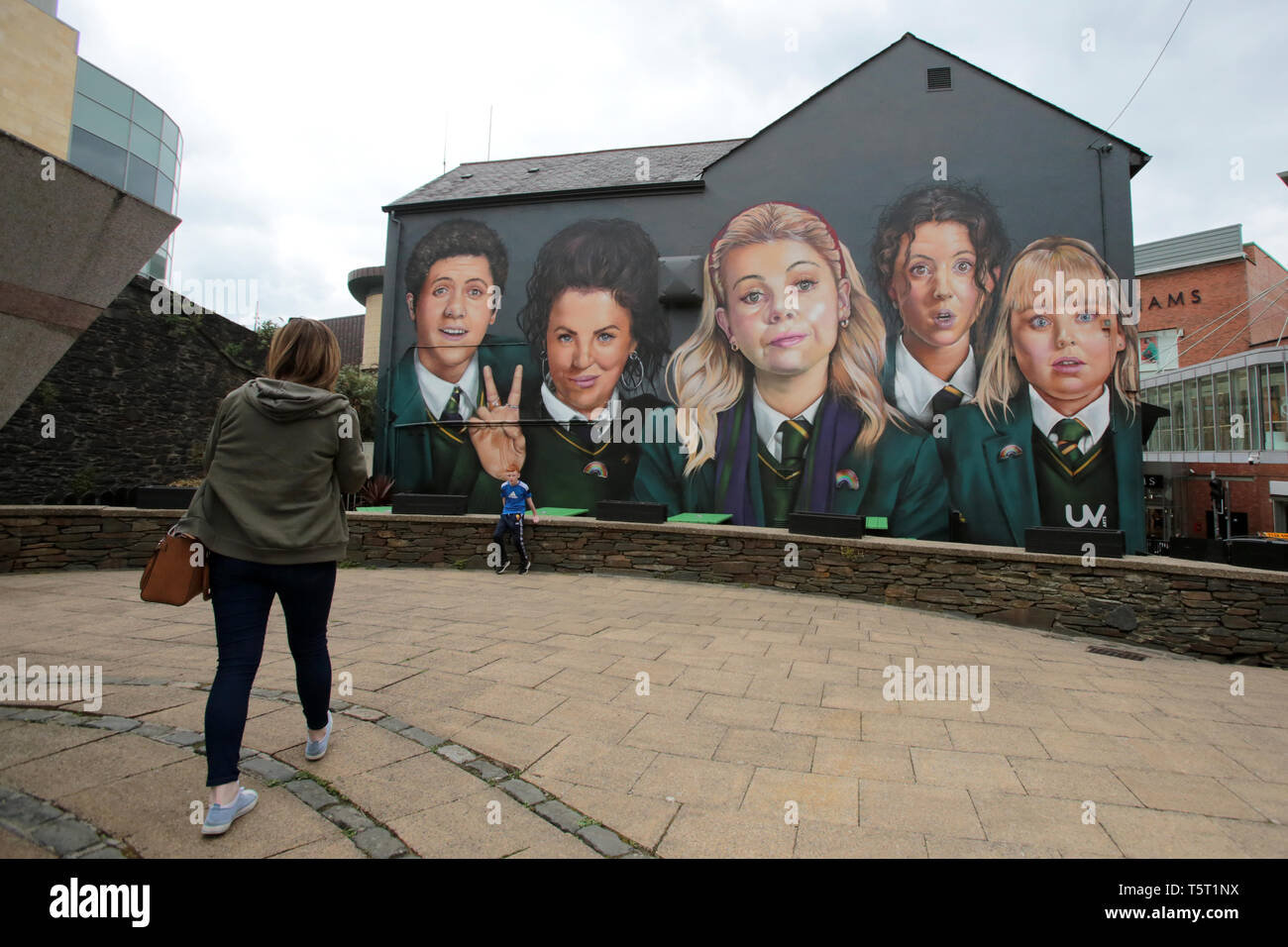 Derry, County Londonderry, Northern Ireland, 25th April, 2019 .A family stops in front of the Channel 4 hit TV show Derry Girls Mural in Derry/Londonderry, Northern Ireland. Derry Girls is a British television sitcom created and written by Lisa McGee. Staring Erin (Saoirse-Monica Jackson), her cousin Orla (Louisa Harland) and their friends Clare (Nicola Coughlan), Michelle (Jamie-Lee O'Donnell) and Michelle's English cousin James (Dylan Llewellyn) navigate their teen years during the Troubles in Derry, where they all attend a Catholic girls' secondary school. Erin lives with her father, Gerry; Stock Photo