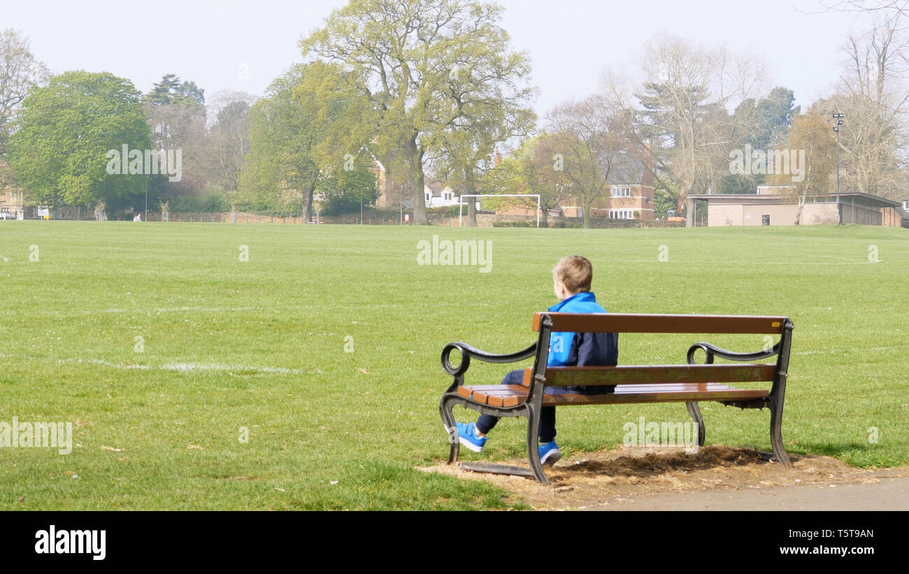 Teen Boy Sitting On Bench In Empty British Park Dressed In