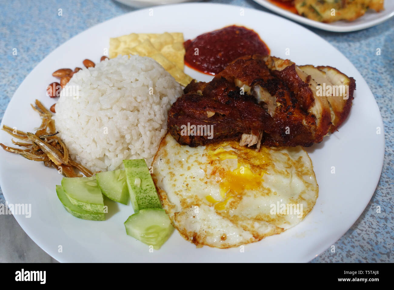 Nasi Lemak, Malaysian coconut rice served with fried egg, cucumber, fried anchovies, peanuts and fried chicken cooked in chili sauce Stock Photo