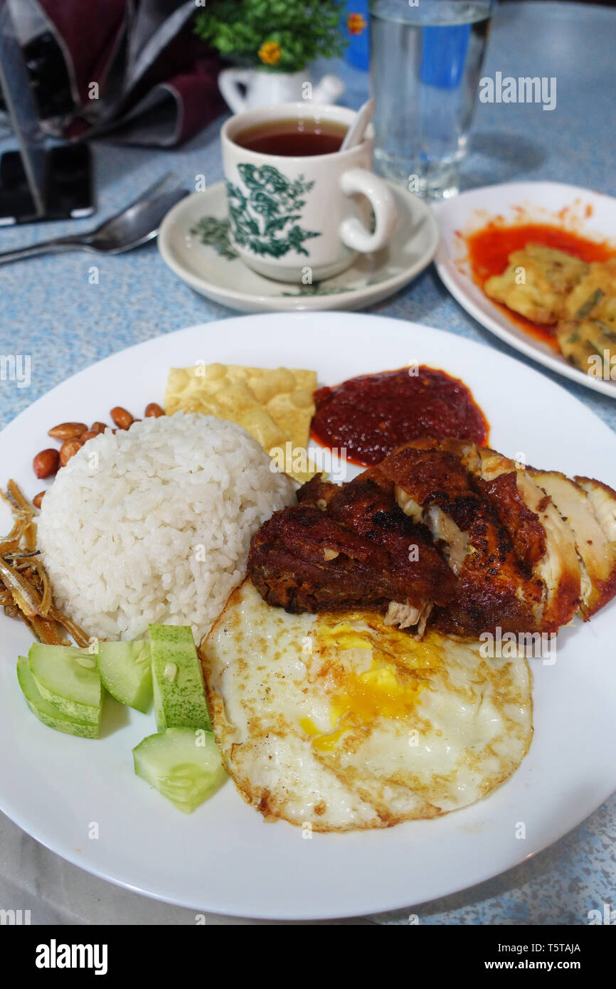 Nasi Lemak, Malaysian coconut rice served with fried egg, cucumber, fried anchovies, peanuts and fried chicken cooked in chili sauce Stock Photo