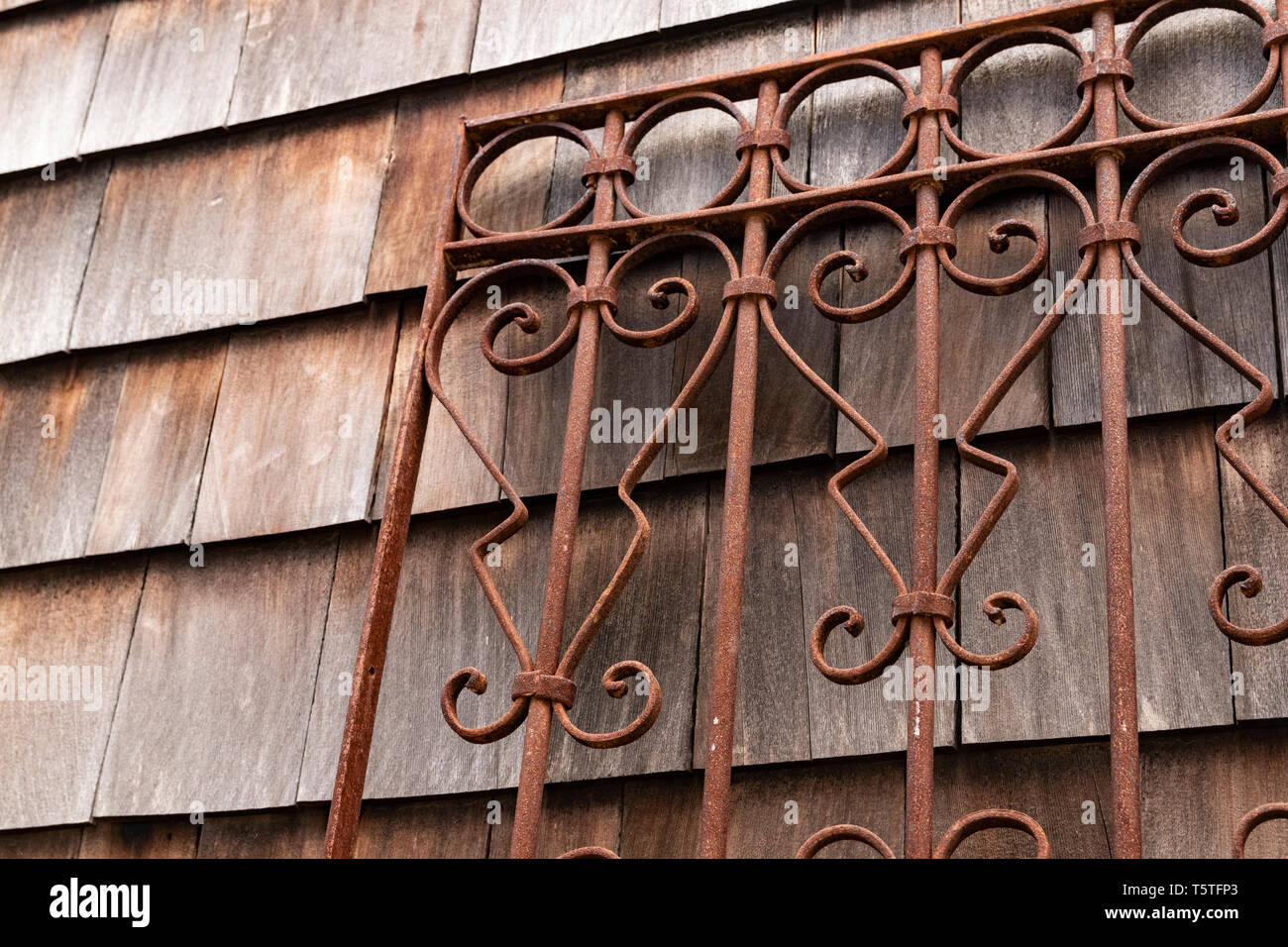 Weathered wood shingle siding and rusty wrought iron metal gate Stock Photo