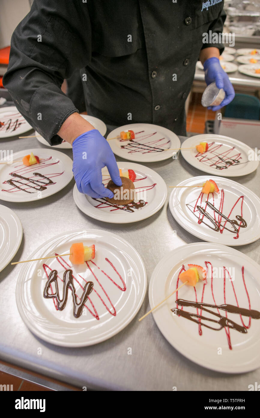 dessert plates in a kitchen being prepared for guests at a celebarion, lines of chocolate and strwberry sauce on the plate Stock Photo