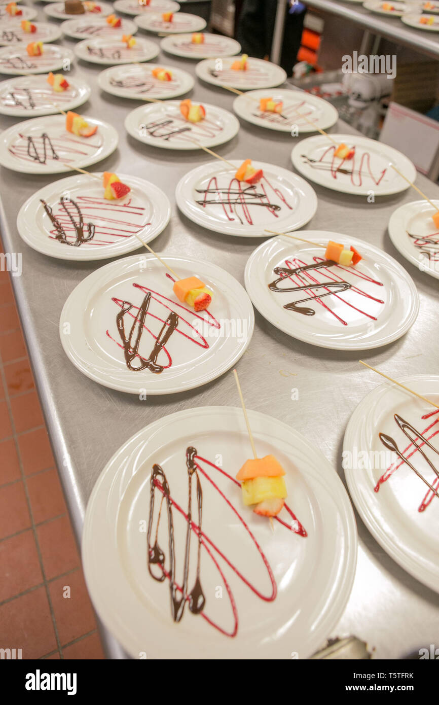 dessert plates in a kitchen being prepared for guests at a celebarion, lines of chocolate and strwberry sauce on the plate Stock Photo