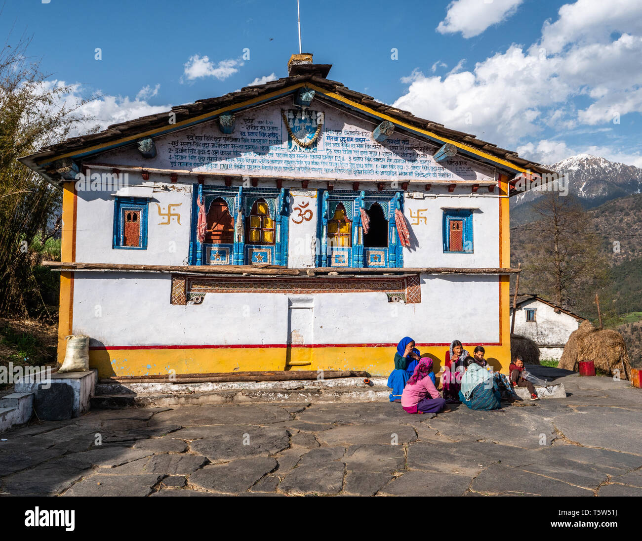 A group of villagers sitting by the colourful principal house in Supi village high up in the Saryu Valley of the Uttarakhand Himalayas northern India Stock Photo