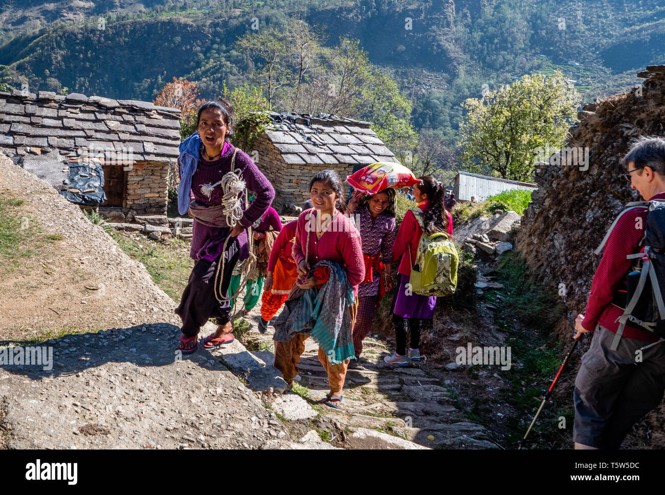 Happy smiling women and children passing a European walker on the steep path in the village of Supi in the Uttarakhand Himalayas of Northern India Stock Photo