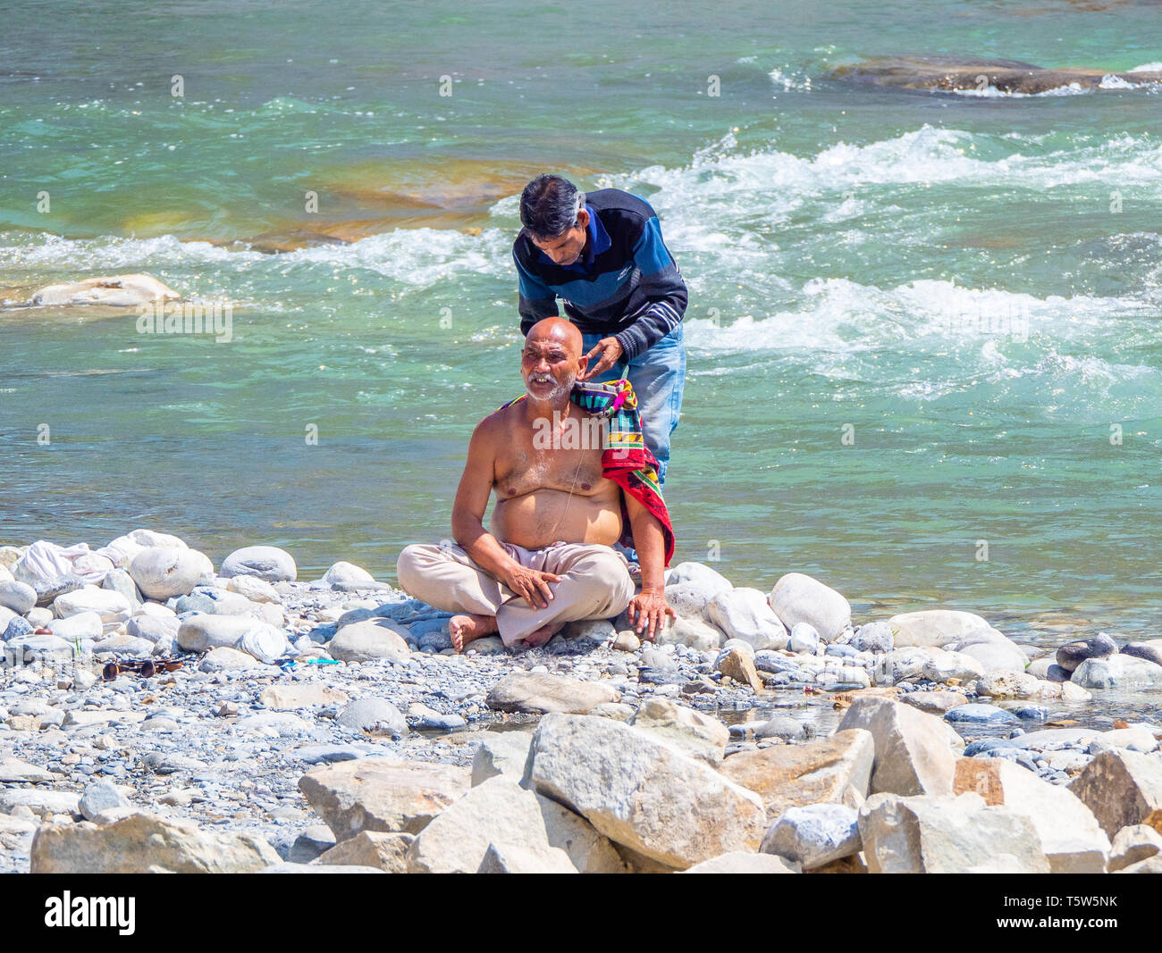 Man having his head shaved by the fast flowing waters of the sacred Saryu River in Bageshwar in Northern India Stock Photo