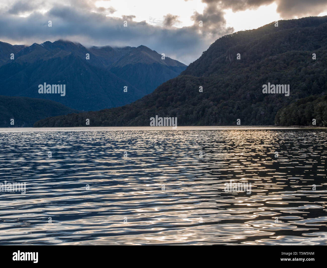 Ripples of blue evening light, calm water, wild mountain landscape, steep slopes, Lake Hauroko, Fiordland National Park, Southland, New Zealand Stock Photo
