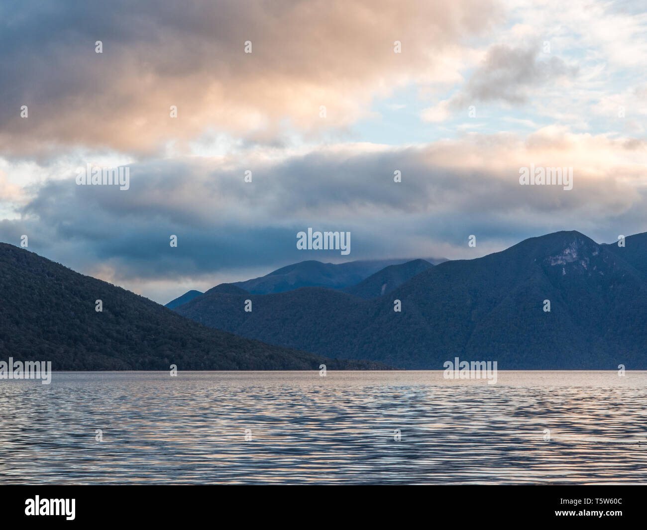 Autumn evening, a distant view, light ripples on calm water, clouds over dark mountains, Lake Hauroko, Fiordland National Park, Southland, New Zealand Stock Photo