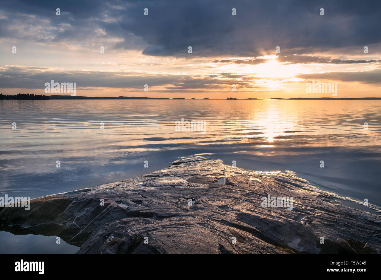 Scenic sunset with peaceful lake and rock at spring evening in Finland Stock Photo