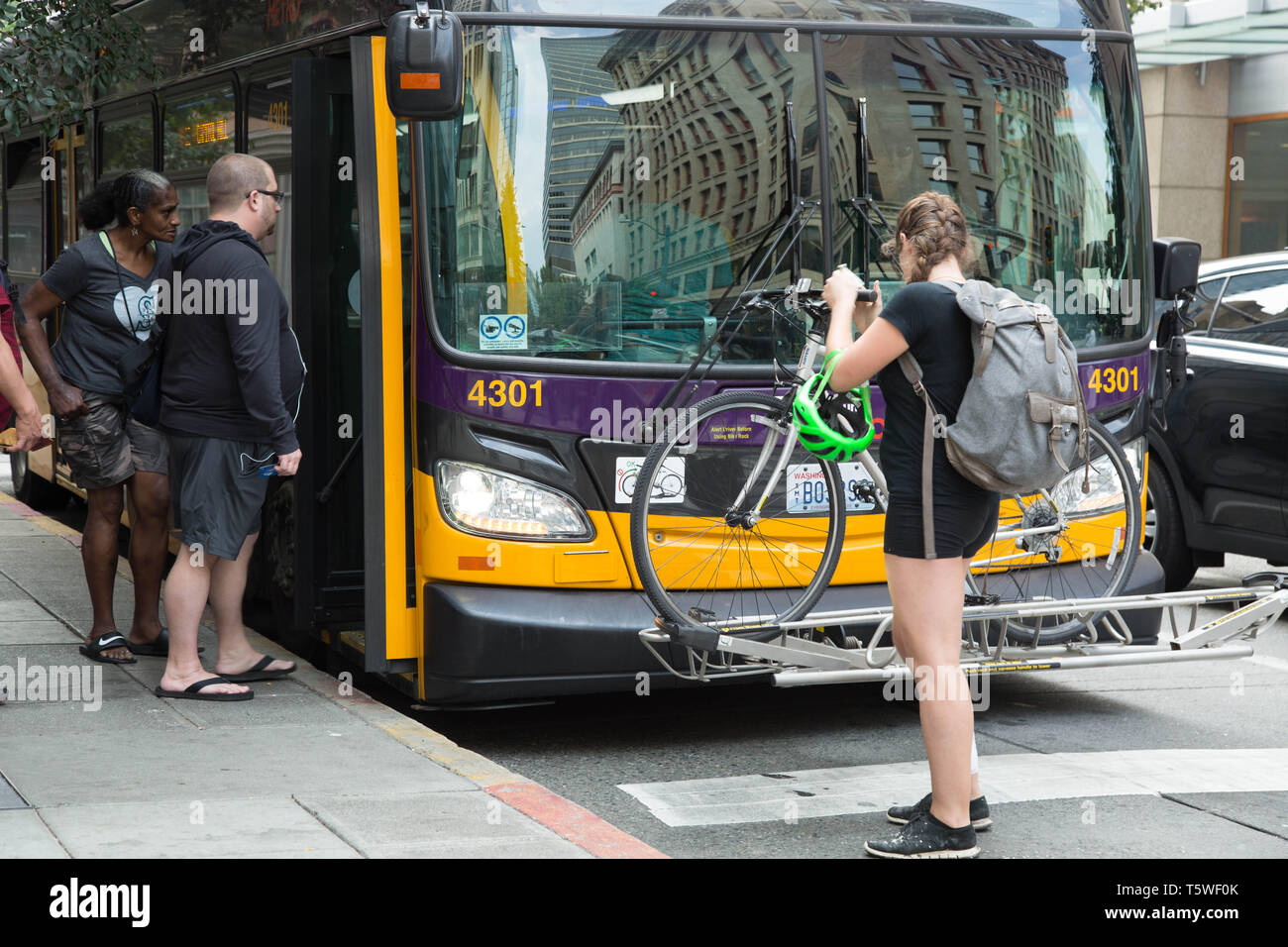 People catching a city bus waiting in turns and one young woman loading up her bicycle on the front of the bus in downtown, Seattle, USA. Stock Photo