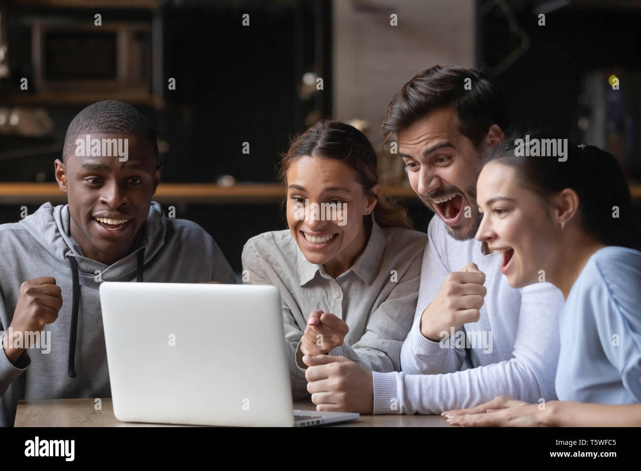 Diverse friends watching online game at laptop in public place Stock Photo