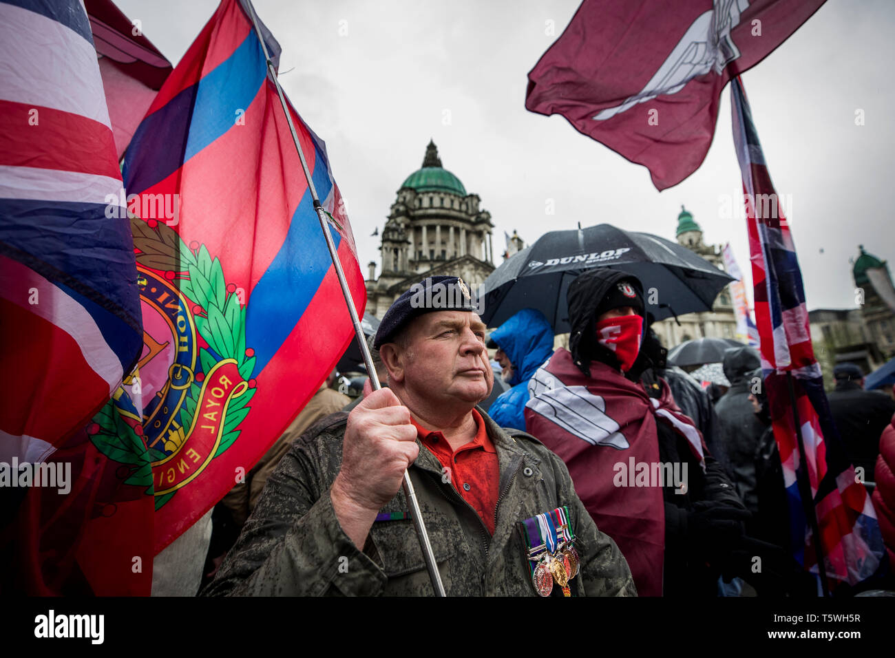 British army veteran stands holding the flag of Royal Engineers as he joins protesters outside Belfast City Hall, at a rally for a former paratrooper, soldier F, who is due to stand trial for murder and attempted murder for his role in the 1972 Bloody Sunday killings. Stock Photo