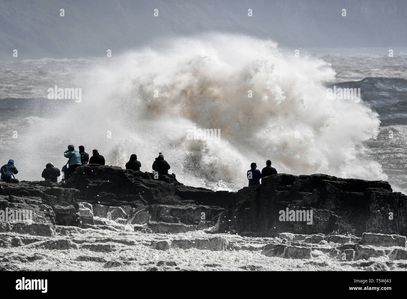 People watch huge stormy waves crash against the shore at Porthcawl, Wales, where Storm Hannah is creating extremely strong gusts of wind. Stock Photo