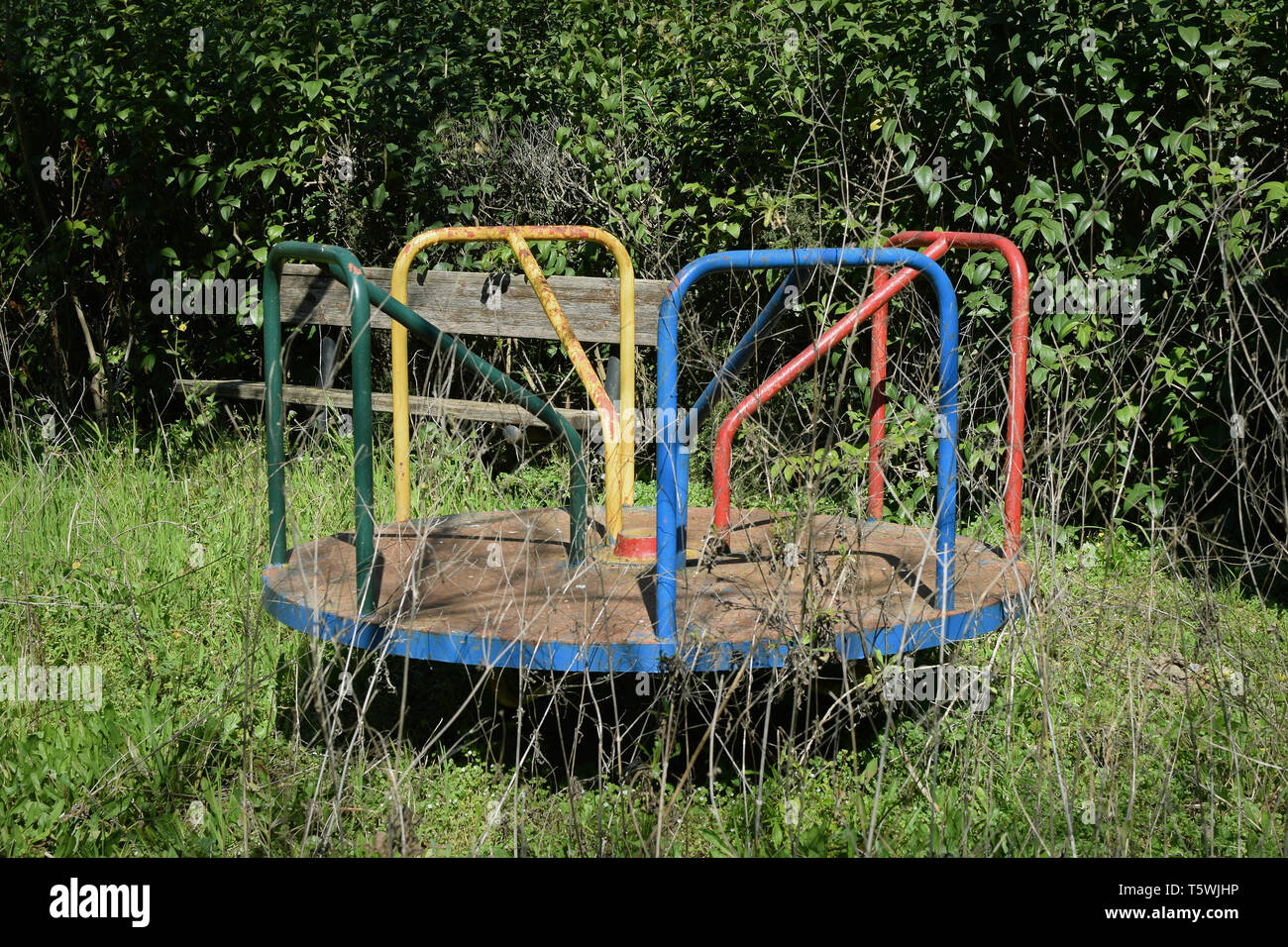Old rusty playground merry-go-round and overgrown withered plants in abandoned park. Stock Photo