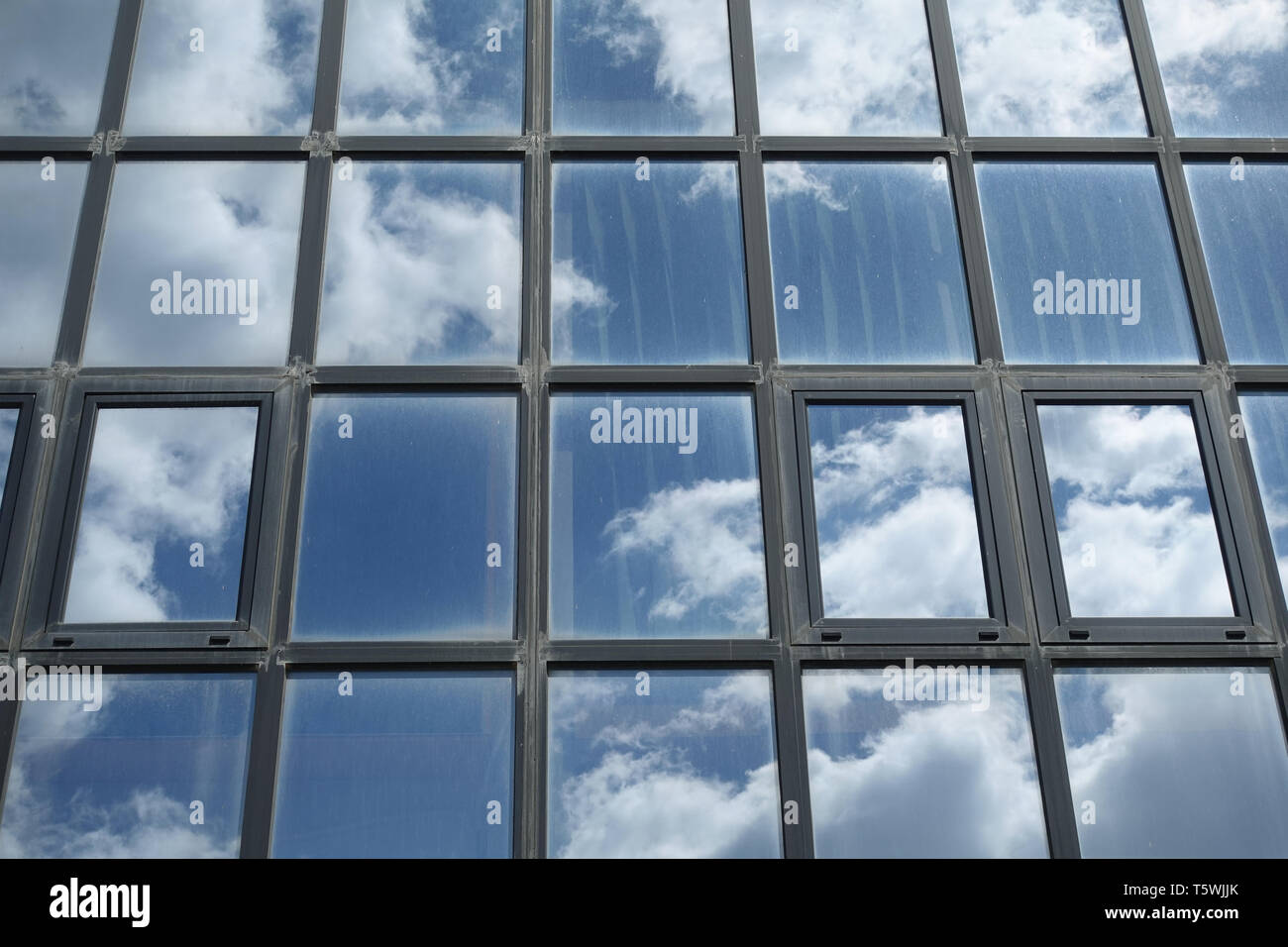 Blue sky and white clouds reflected on dirty windows. Office building facade closeup abstract background. Stock Photo
