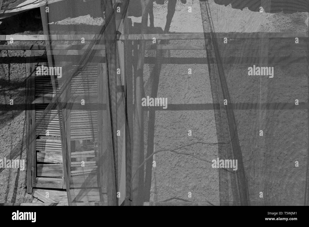 Broken window behind transparent debris netting. Abandoned house black and white. Stock Photo