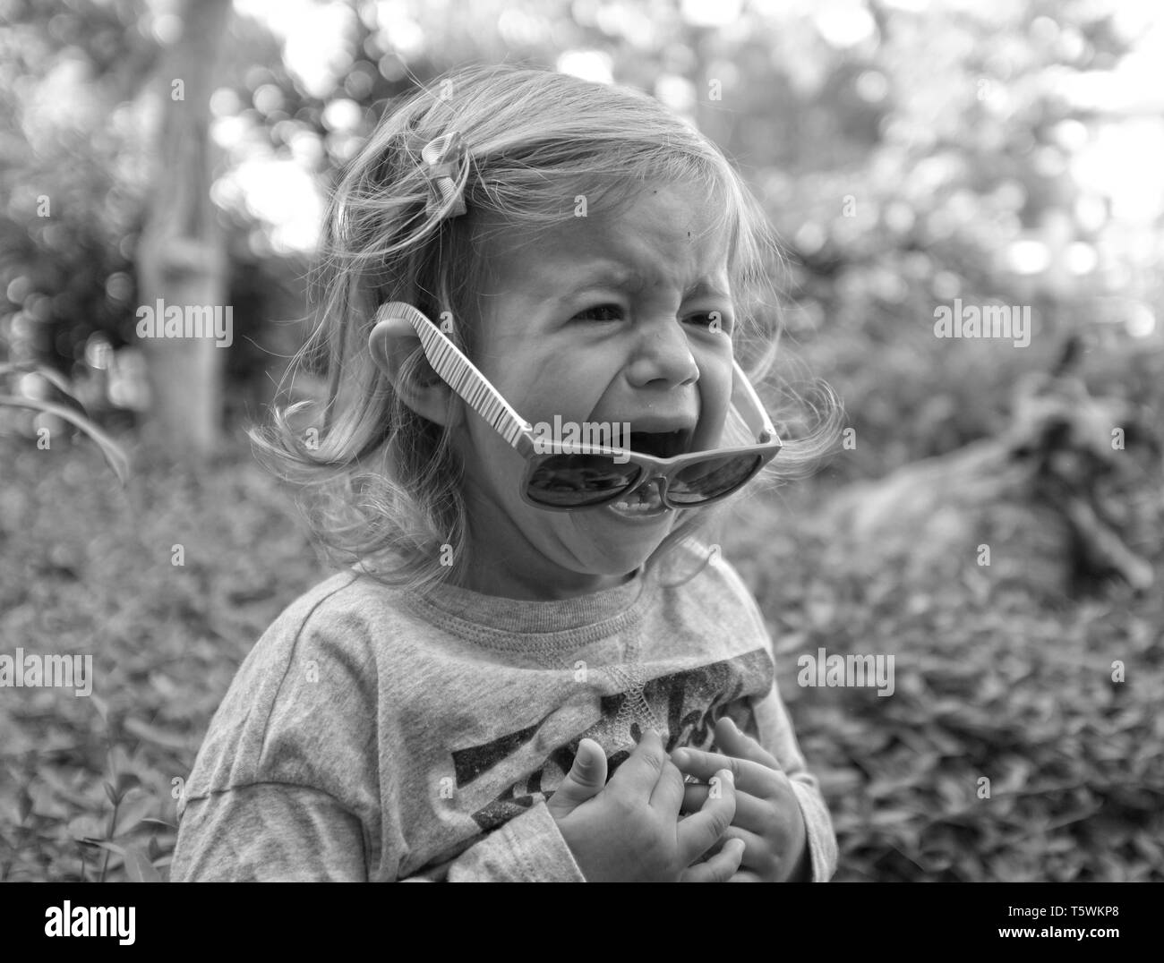 Little girl crying in the garden on spring background. Sad and angry concept. Stock Photo