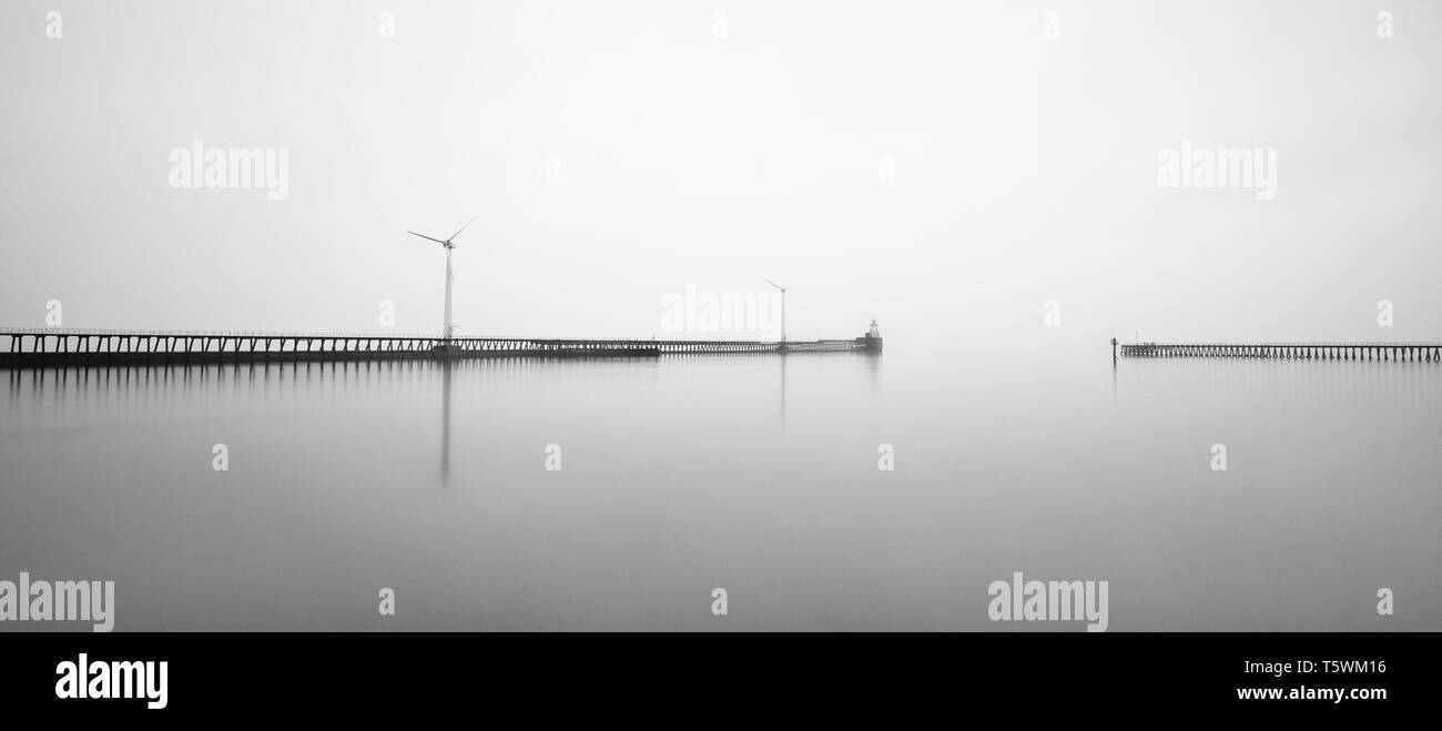 No sunrise on this morning at Blyth piers, but the coastline was surrounded by thick fog which made for some atmospheric looking B&W on Wind turbines Stock Photo