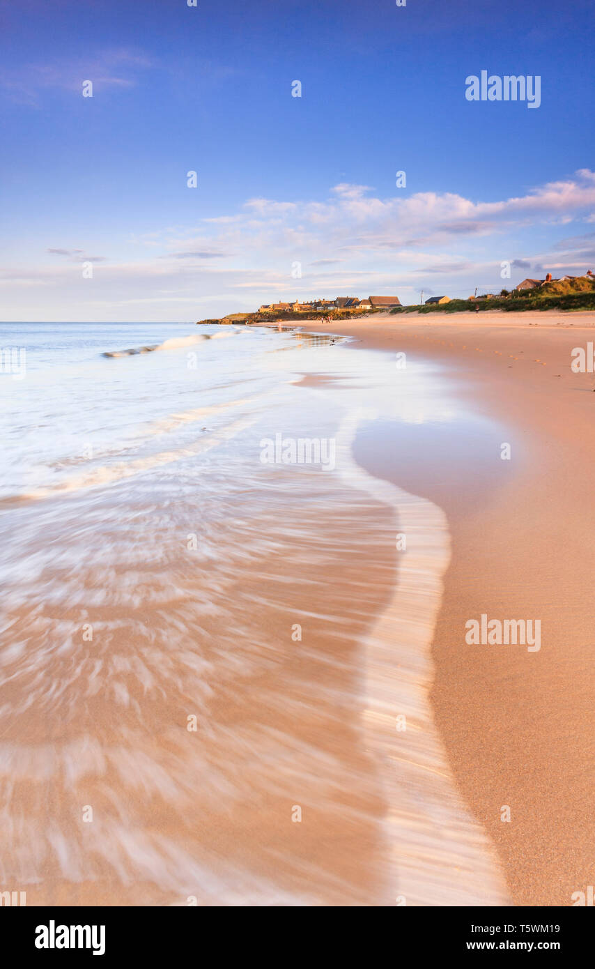 Standing in the breaking surf of the sea on warm summers evening sunset looking back towards Cresswell with reflection of the scenery in the water Stock Photo
