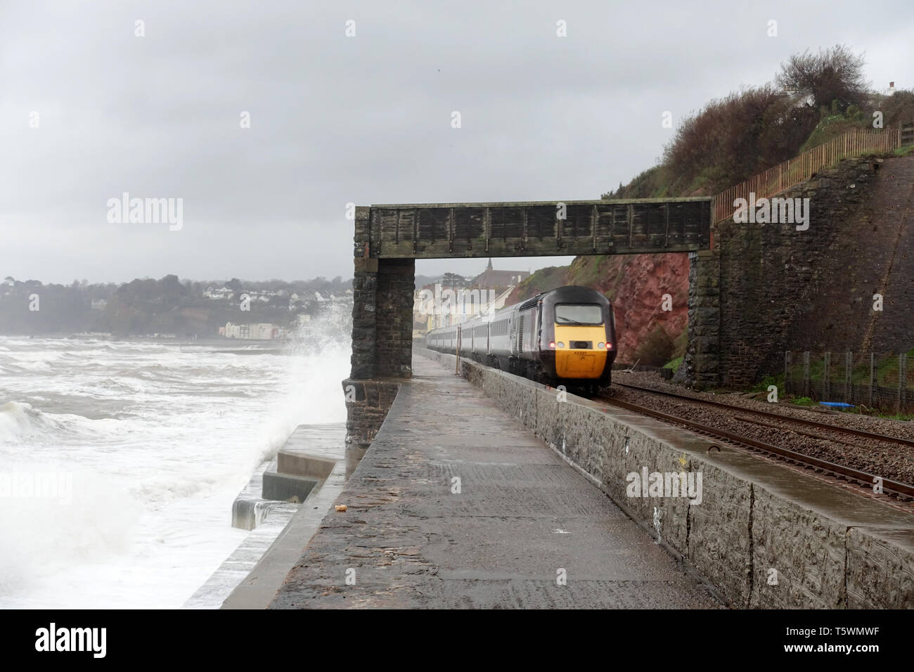 A high speed inter city diesel train travelling at speed along the train track at Dawlish, Devon, UK. There’s a stormy sea as high winds hit the coast Stock Photo