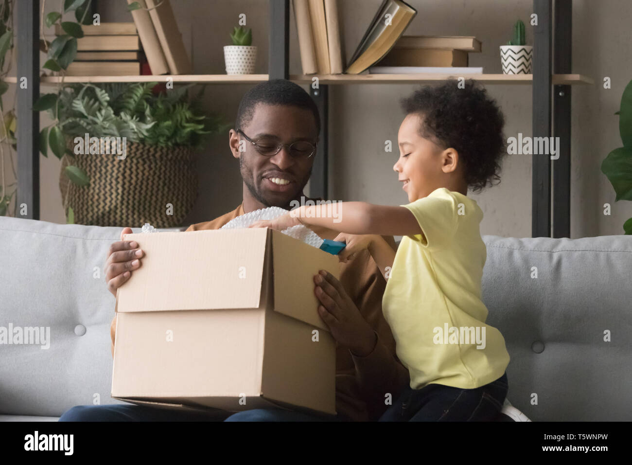 Happy african father and little son opening parcel at home Stock Photo