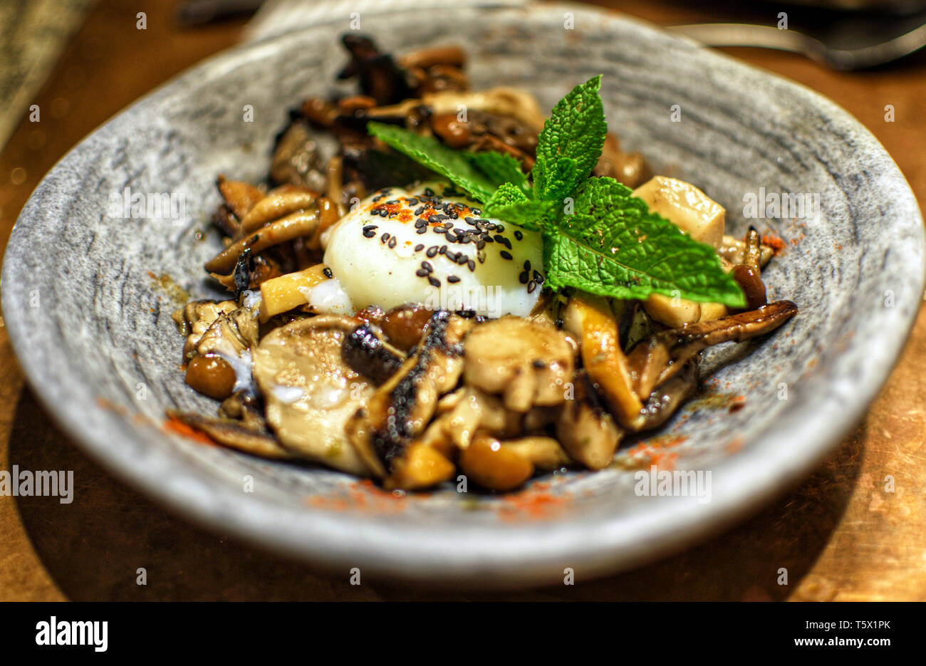 A bowl of mushrooms and fungi with an egg cooked at low temperature. Modern cuisine in Spain 2019. Low tempered egg with mushroom,  toadstool served with a mint leaf. Stock Photo