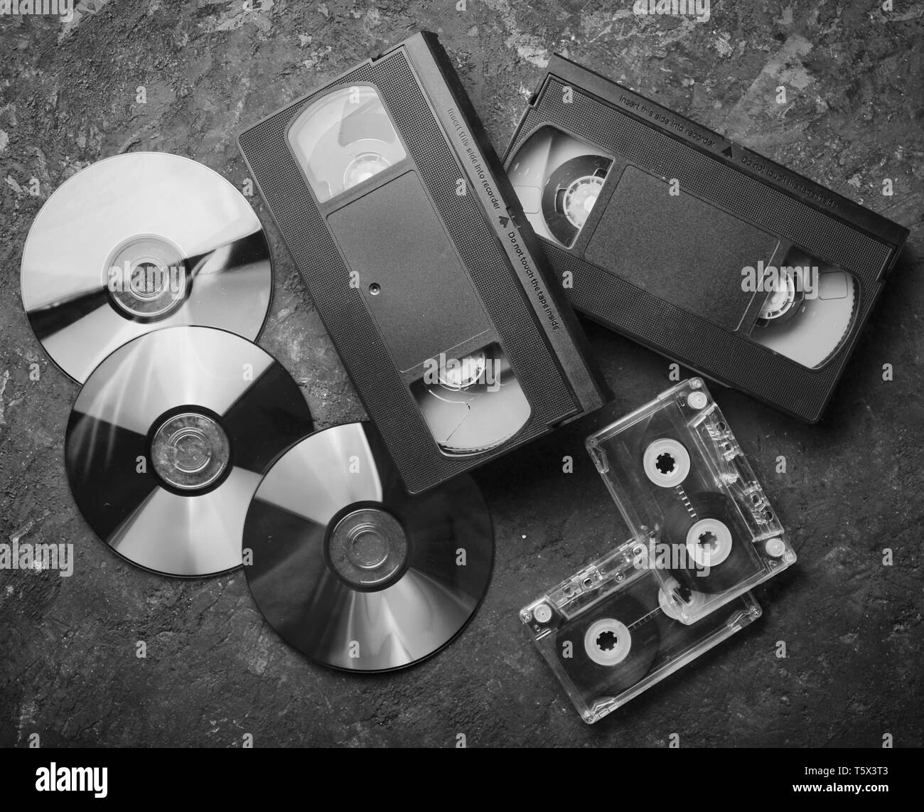 Entertainment and media technology from the 90s. CD's, audio cassettes, video cassettes on a black concrete surface. Top view. Stock Photo