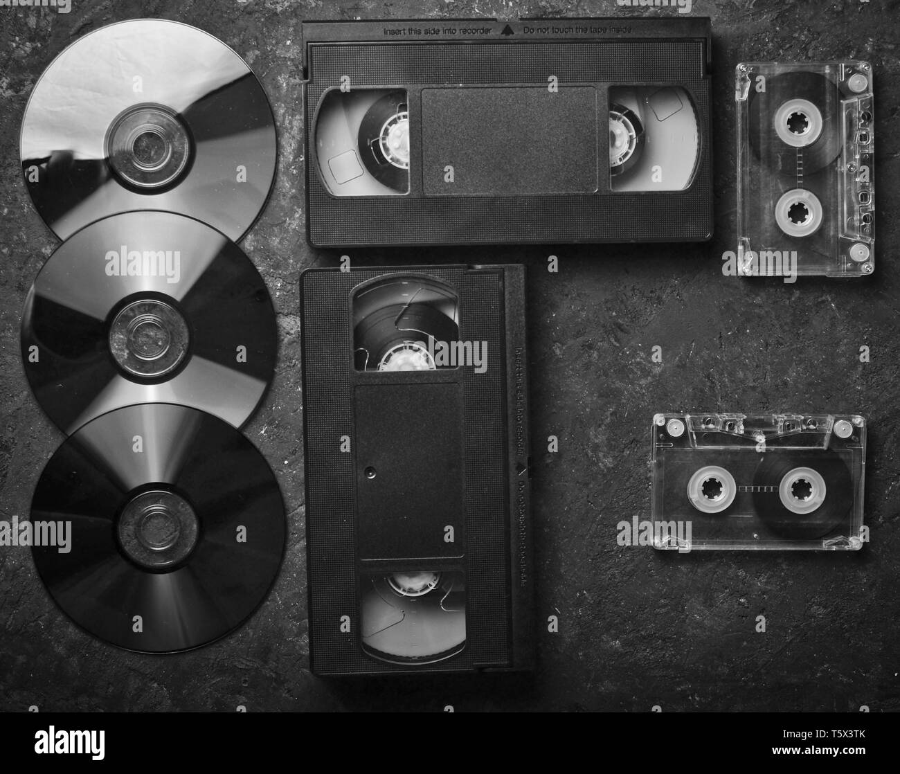 Flat lay video cassettes, CD's, audio cassette on a black concrete surface. Retro media technology of the past. Top view. Stock Photo