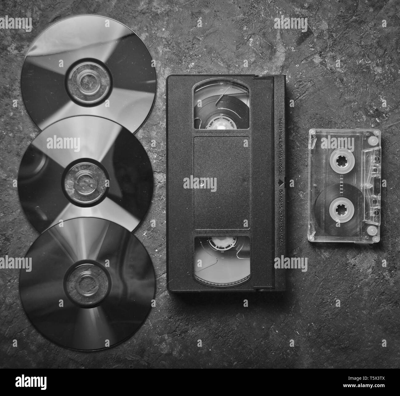 Flat lay video cassettes, CD's, audio cassette on a black concrete surface. Retro media technology of the past. Top view. Stock Photo