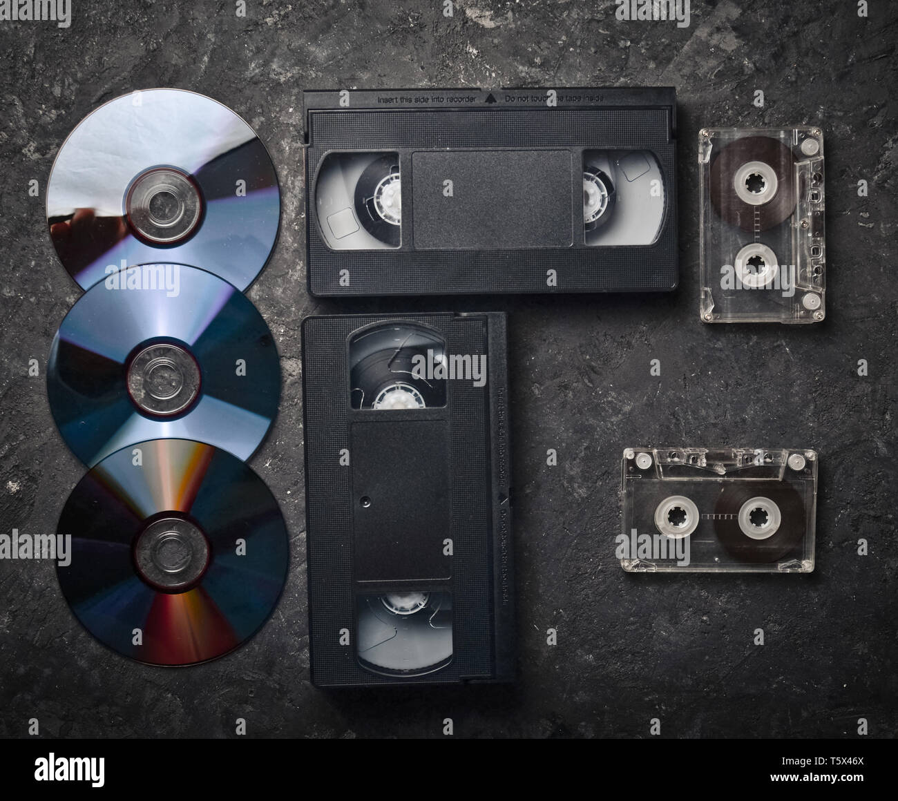 Flat lay video cassettes, CD's, audio cassette on a black concrete surface. Retro media technology of the past. Top view. Stock Photo