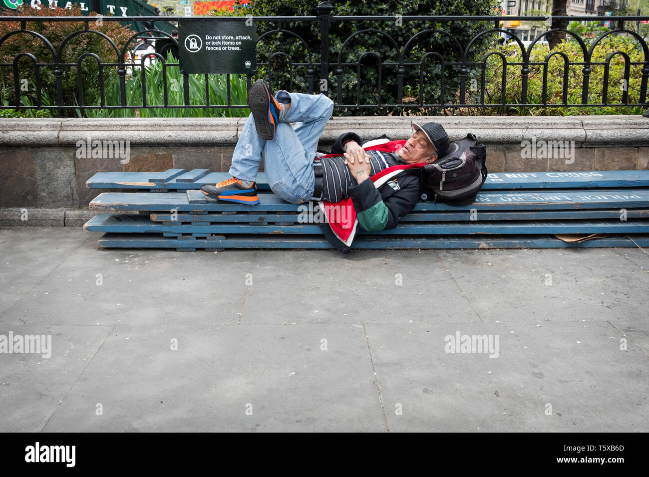 A man having a nap on some wooden planks outsdoors in Union Square Park in lower Manhattan, New York City. Stock Photo
