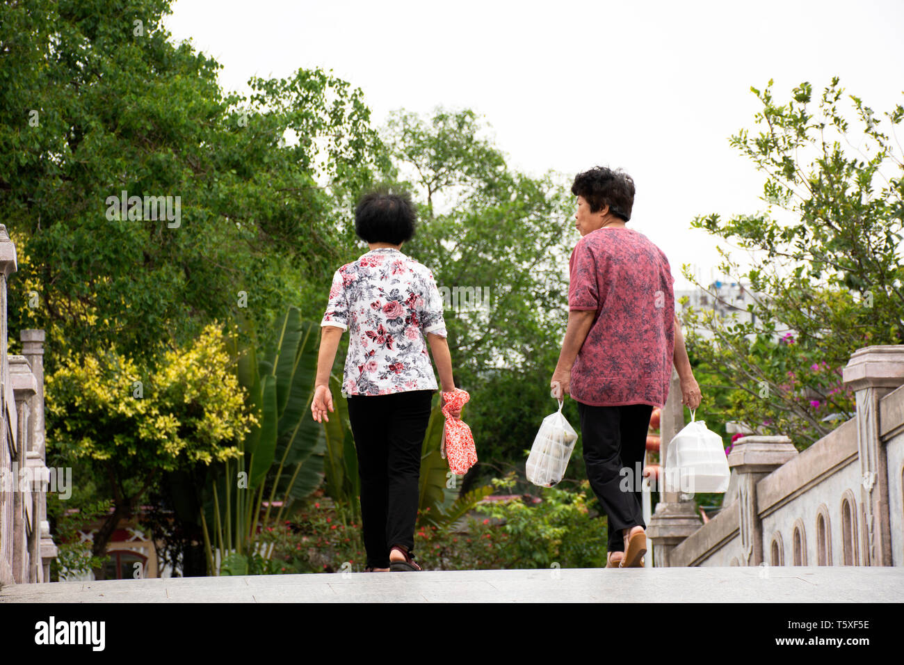 Chinese old women people walking holding food in plastic bag relaxing on bridge in garden at Zhongshan Park in Shantou city or Swatow city on May 9, 2 Stock Photo