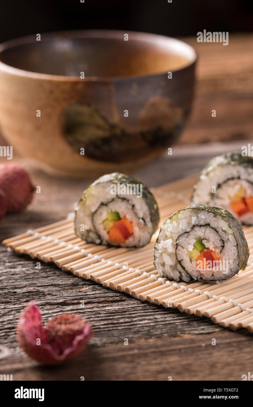 Three maki sushi rolls on bamboo mat on wooden table, traditional asian