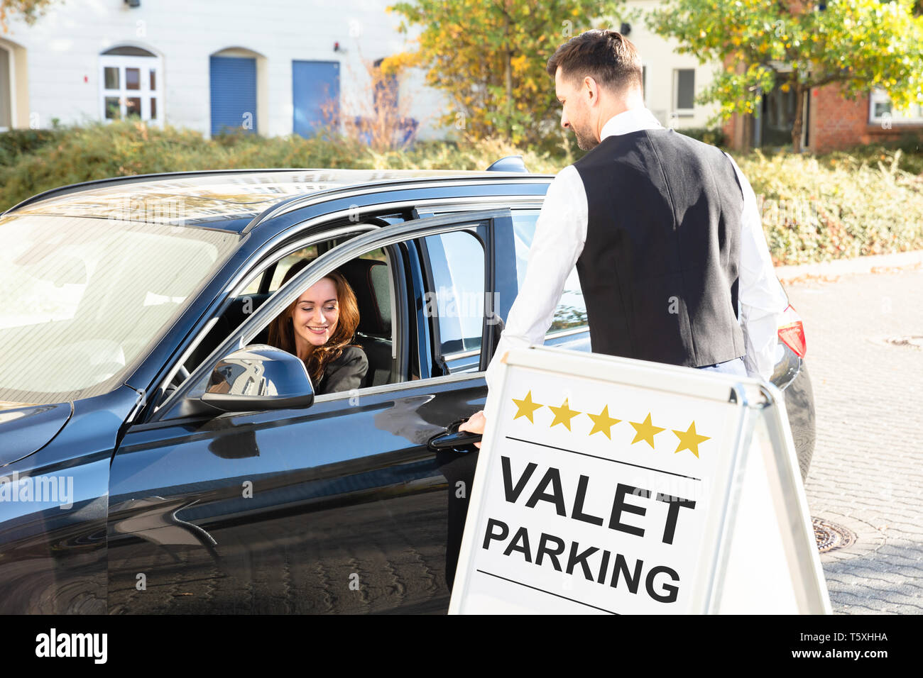 Happy Male Valet Opening Car Door Near Valet Parking Sign Stock Photo
