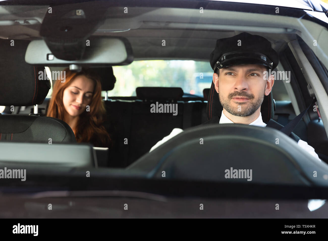 Portrait Of A Smiling Male Chauffeur Driving Car With Businesswoman Stock Photo