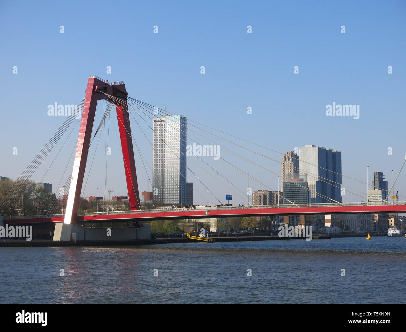 Taken from midway across the Nieuwe Maas, a view of the bright red Willemsbrug bridge and the city of Rotterdam in the background Stock Photo