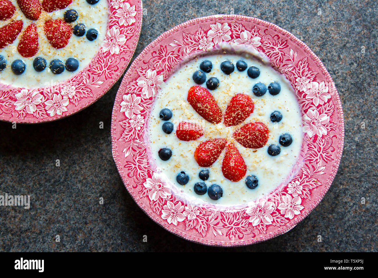 UK breakfast cereal. Old English, ceramic traditional dishes of oatmeal porridge decorated with fresh fruit, strawberries & blueberries. Stock Photo