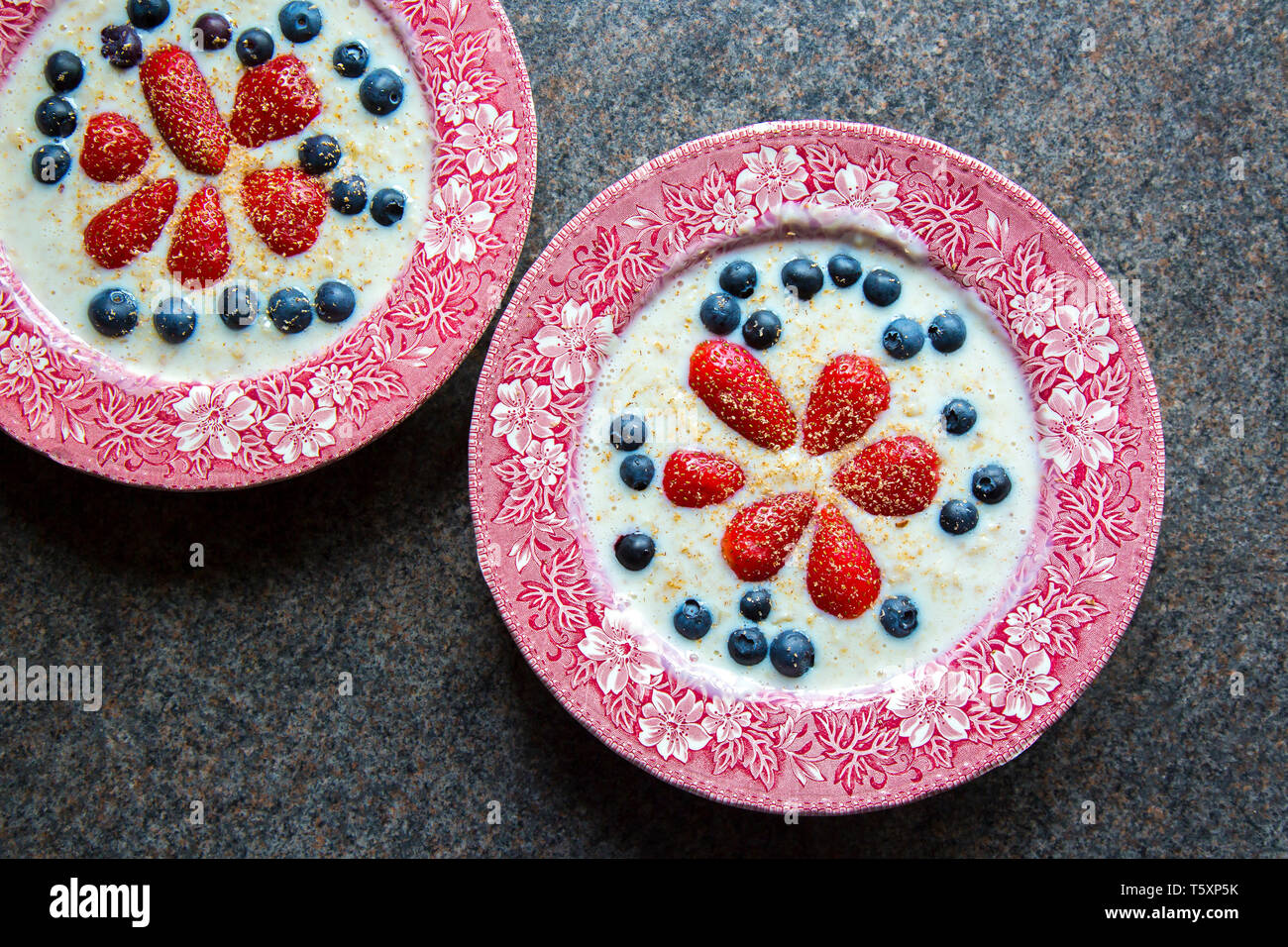 UK breakfast cereal being served: ceramic traditional dishes of oatmeal porridge decorated with fresh fruit, strawberries & blueberries. Stock Photo